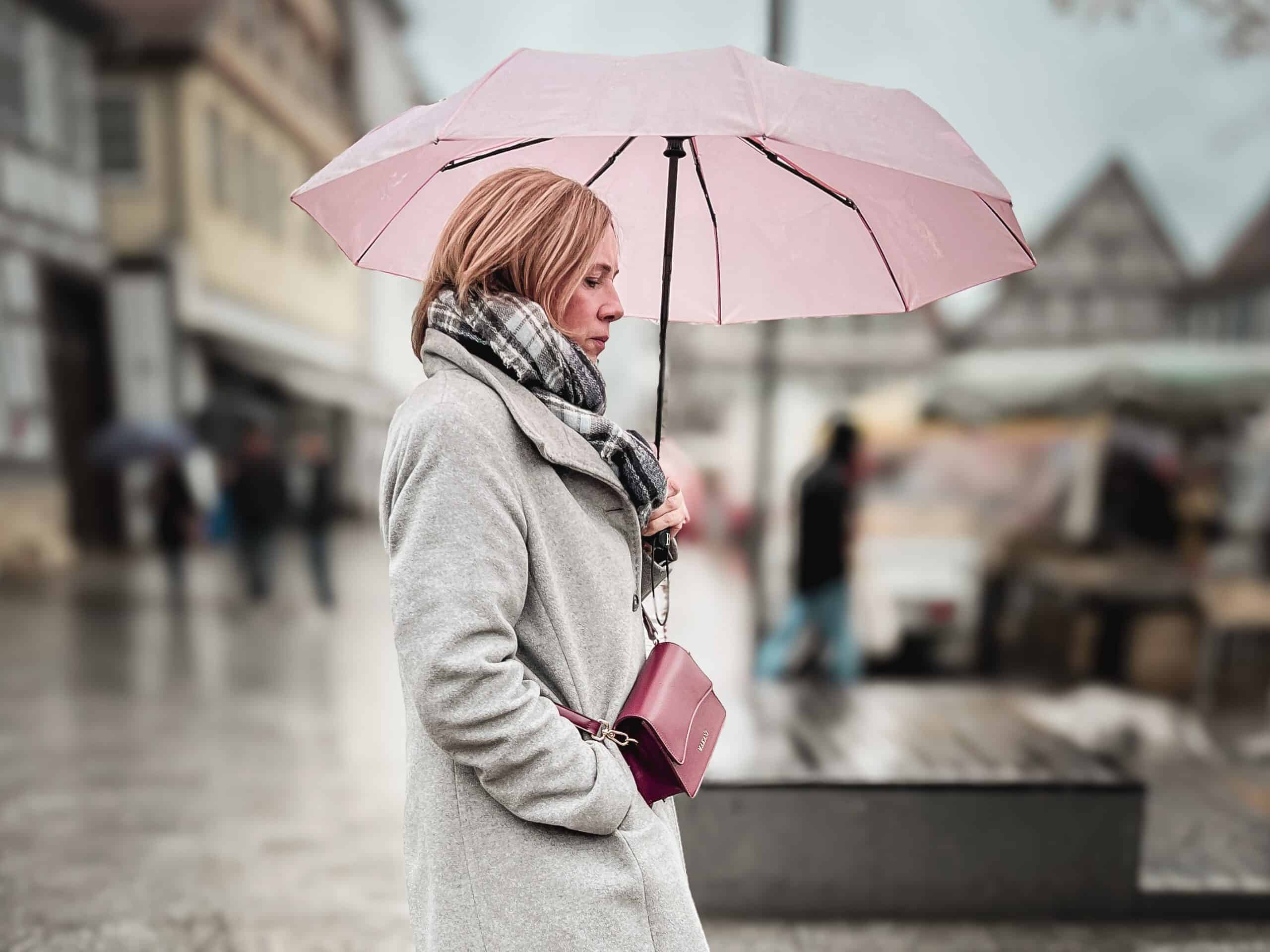 Frau mit pinkem Regenschirm auf nasser Straße, symbolisiert Energie und Wandel in der Midlife-Phase, passend zum Thema "Die Sache mit der Energie".